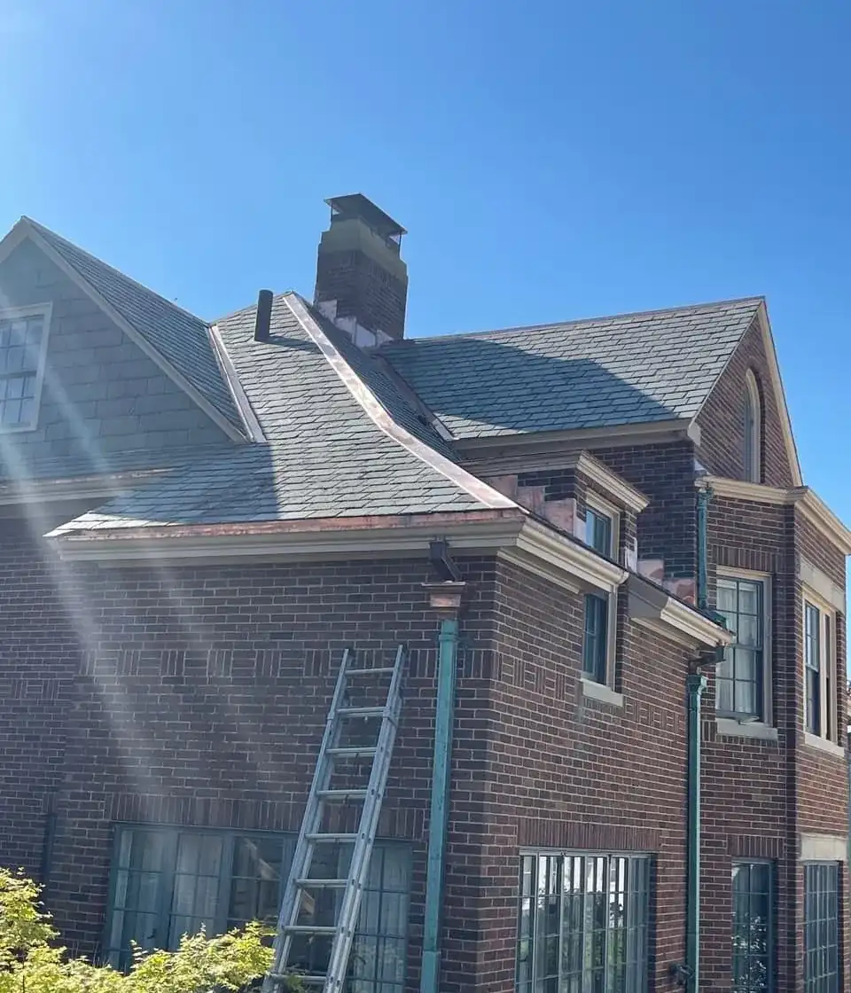 Copper gutters and downspouts with green patina on a brick house with a slate roof