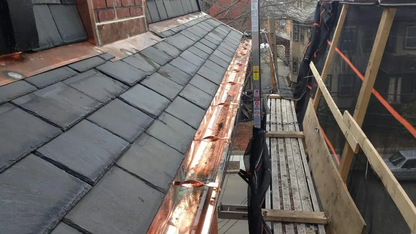 New half round copper gutter on hidden hangers along a slate roof edge, with pump jack staging and debris netting, on an Art Slate project in Back Bay