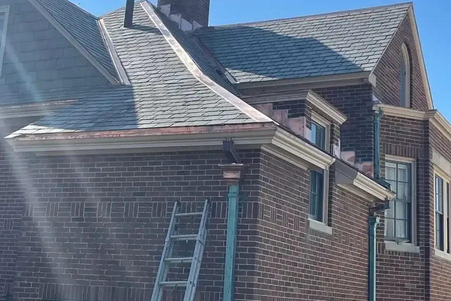 Copper gutters and downspouts on a brick house with a slate roof, where a valley meets the gutter line