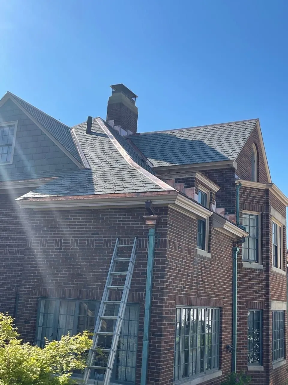 Copper downspouts weathered to a green patina on a brick house with a slate roof and copper trim at the eaves