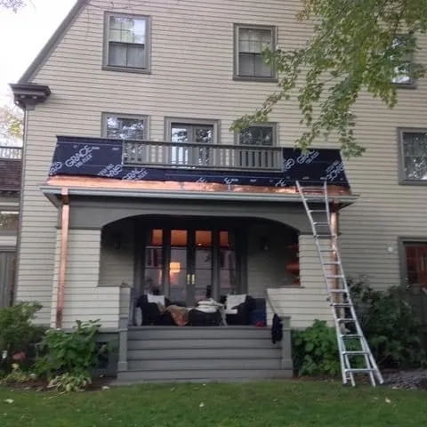 Extension ladder against a porch roof edge trimmed in new copper, with a copper downspout on the corner column